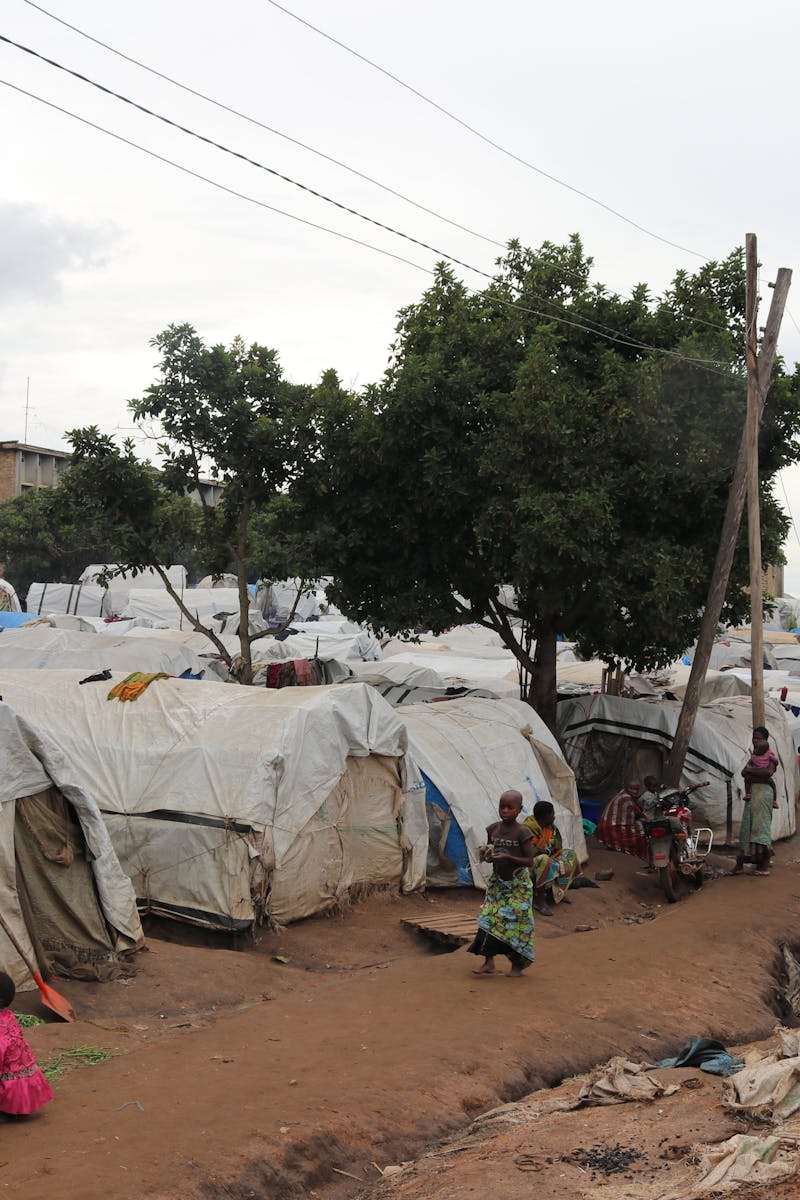Overview of an African refugee camp with families and tents under trees, daytime
